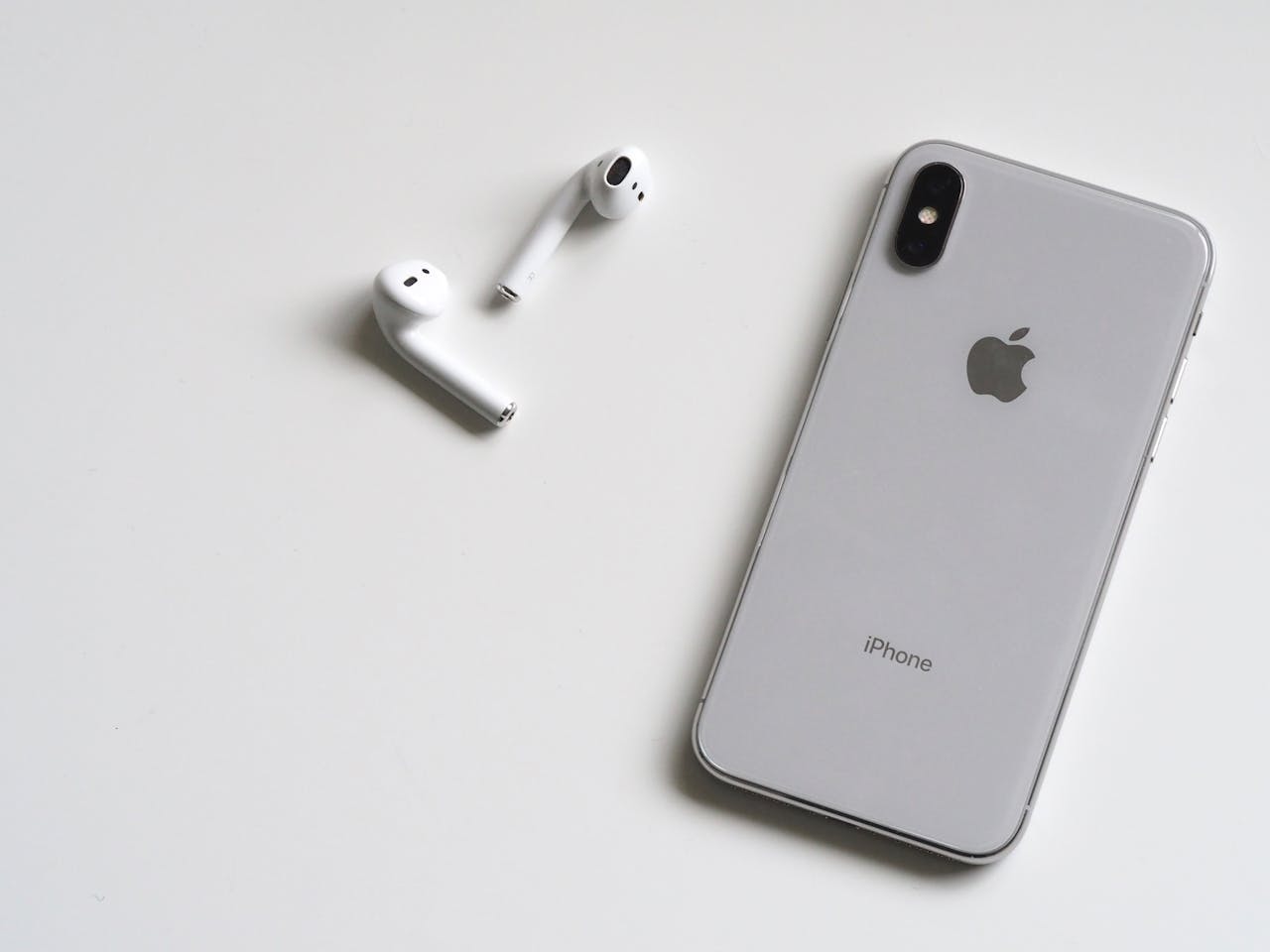 our-story Close-up of a silver iPhone and wireless AirPods on a sleek white background.